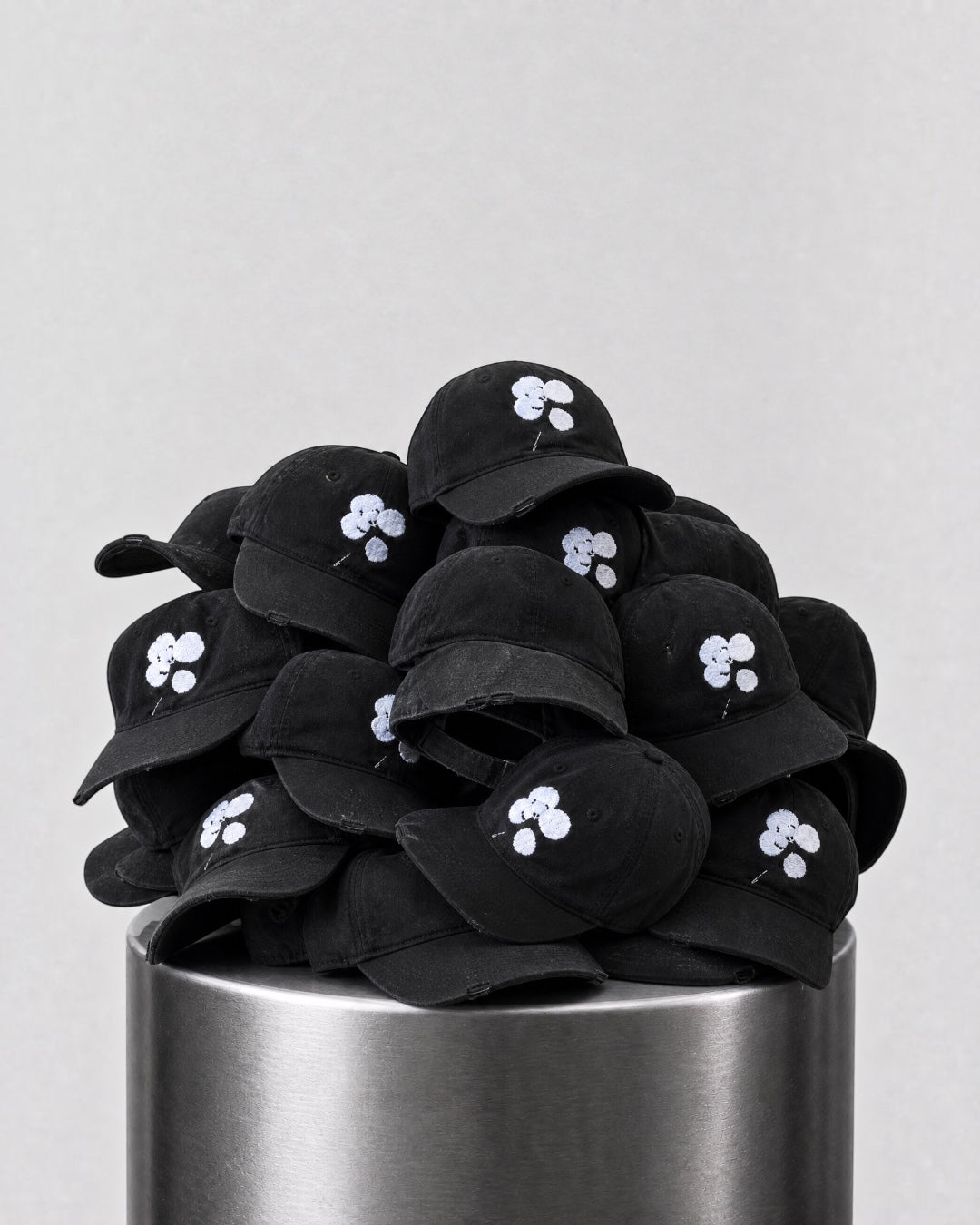 ANTIPROMINDのクローバーロゴが刺繍された黒いコットン製キャップの山。シンプルで洗練されたデザインのベースボールキャップ。