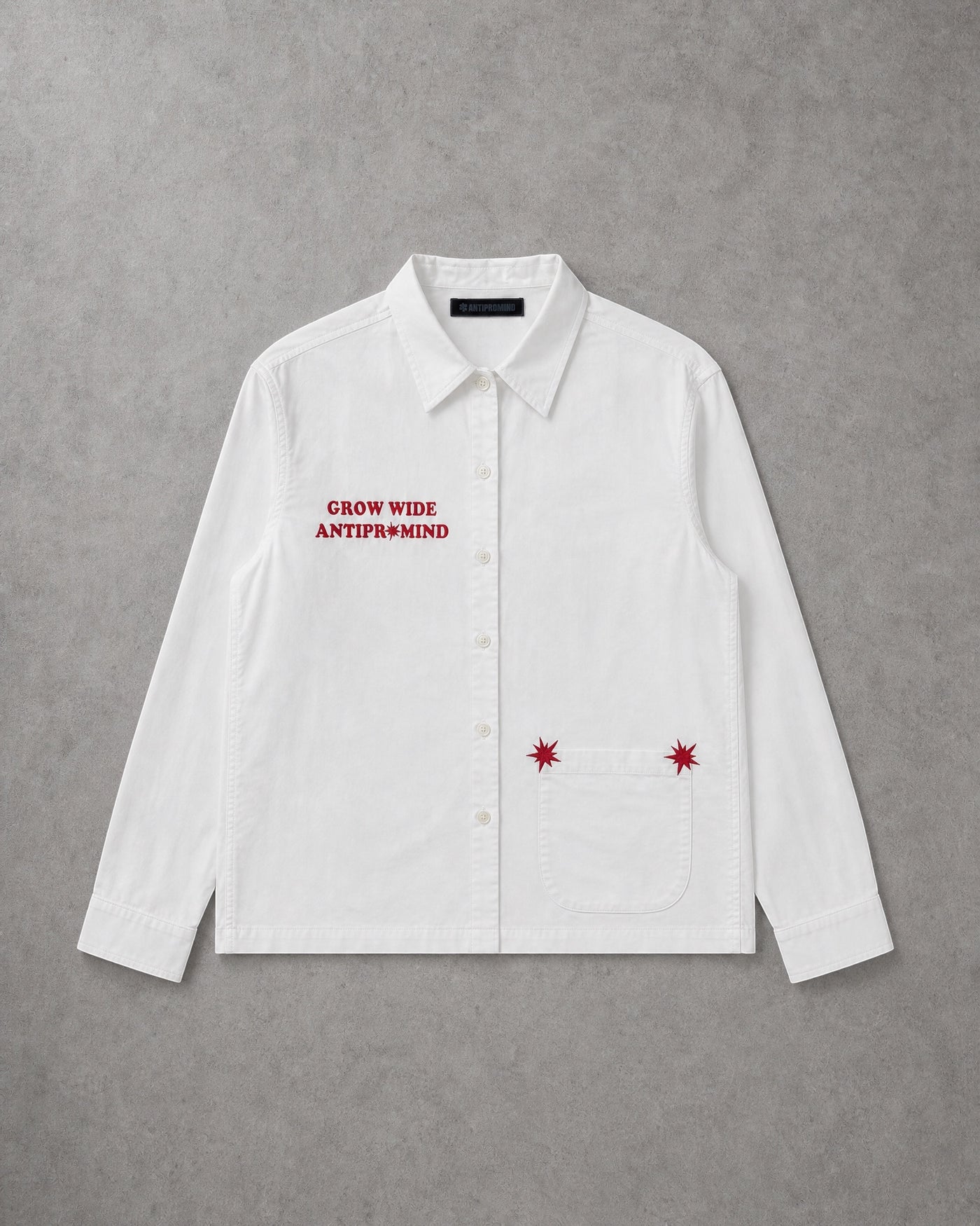 ANTIPROMINDの白いコットン製オープンカラーシャツ。胸元の赤いシリコンプリントとポケットの刺繍が特徴のショート丈スリムフィットシャツ。